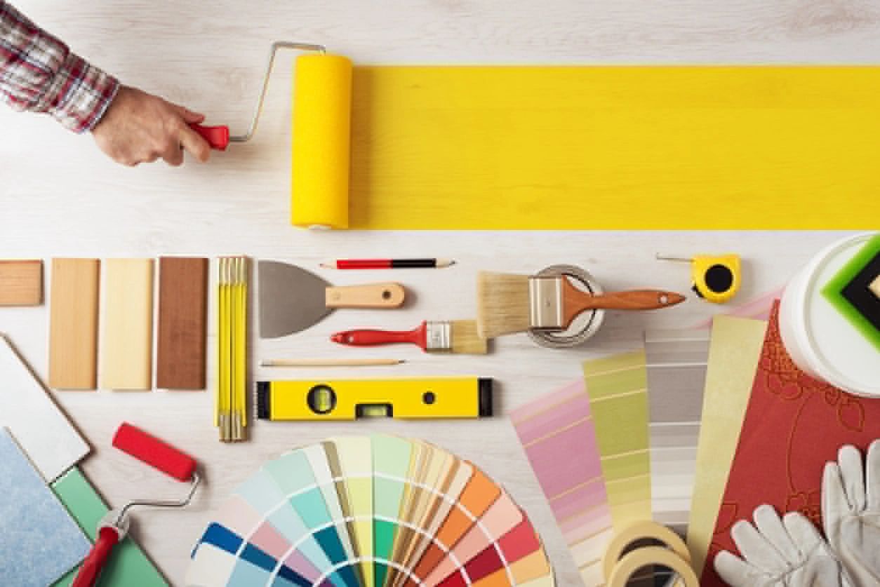 A person holding a paint roller next to some tools.