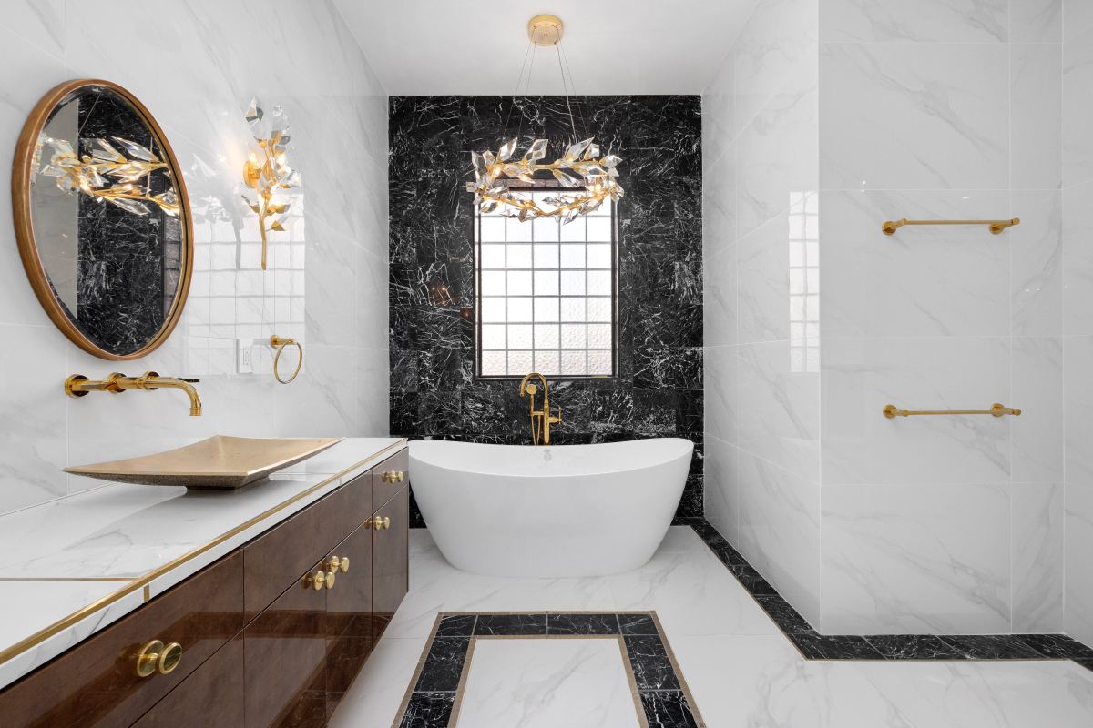 A bathroom with marble walls and floors, a tub, sink and mirror.