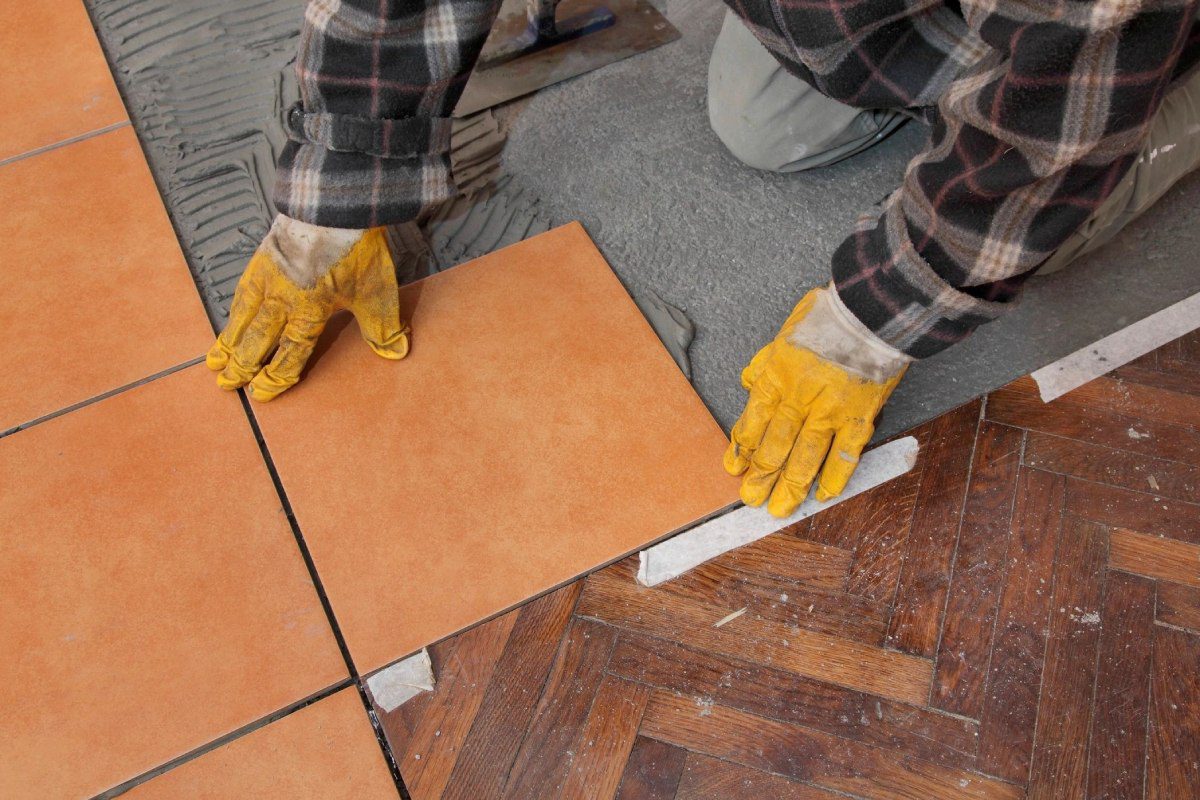 A person with yellow gloves on and holding a tile