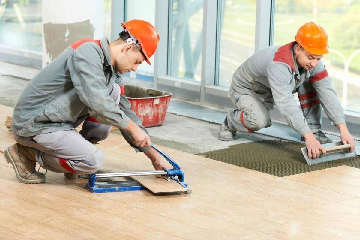 Two men in hard hats working on a floor.