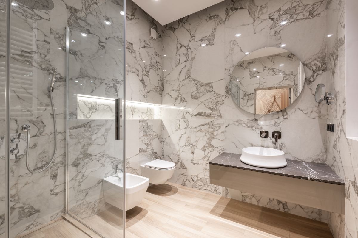 A bathroom with marble walls and floors, and a glass shower door.